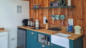 A compact kitchen with teal cabinets, a wooden countertop, a dishwasher, a coffee maker, and a radio. - 1 bedroom accommodation in Ryde (Ryde)