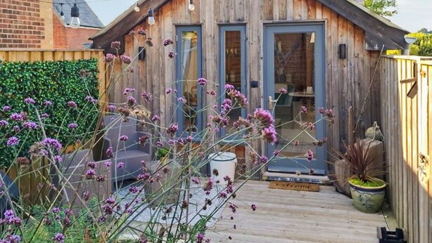 A rustic wooden cabin with a welcoming entrance, a small porch, and a garden area with purple flowers. - 1 bedroom accommodation in Ryde (Ryde)
