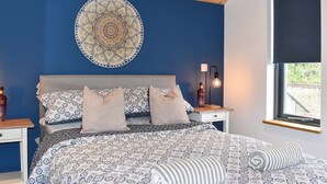 A bedroom with a patterned bedspread, a circular wall hanging, a bedside lamp, and a bottle on the nightstand. - 1 bedroom accommodation in Ryde (Ryde)
