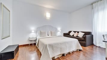 A bedroom with a bed, a nightstand, a lamp, a sofa, and a small table.