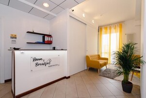 Et receptionsområde med et skilt, der viser 'Room & Breakfast', og en gul lænestol.