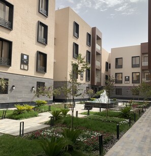 Un bâtiment moderne doté de nombreux balcons et d’une cour aménagée avec une fontaine.
