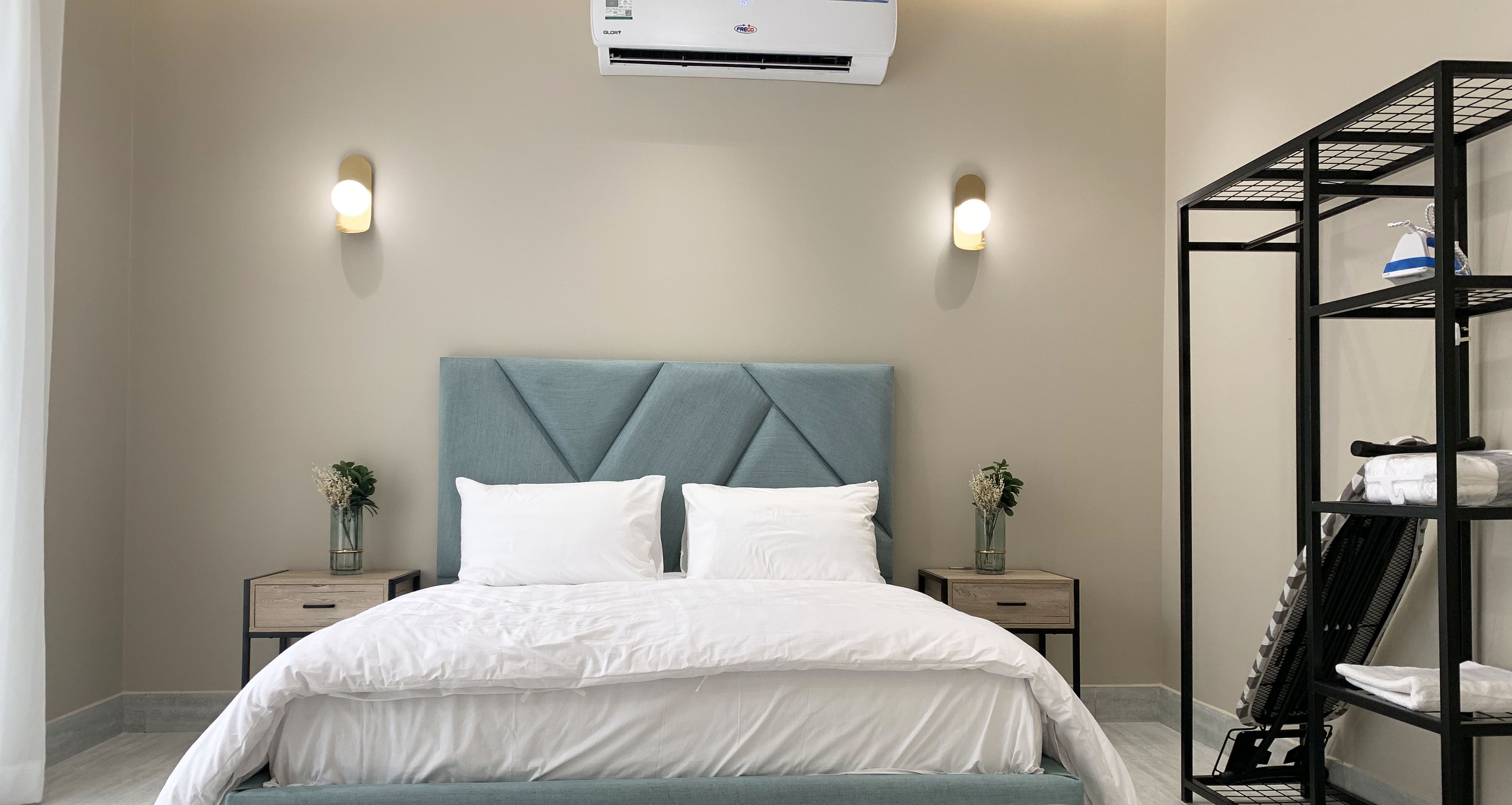 A modern bedroom with a bed, bedside tables, an air conditioning unit, and a built-in shelving unit.