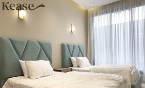Une chambre d’hôtel avec deux lits, chacun doté d’une tête de lit capitonnée, de linge de lit blanc et d’une grande fenêtre ornée de rideaux légers.