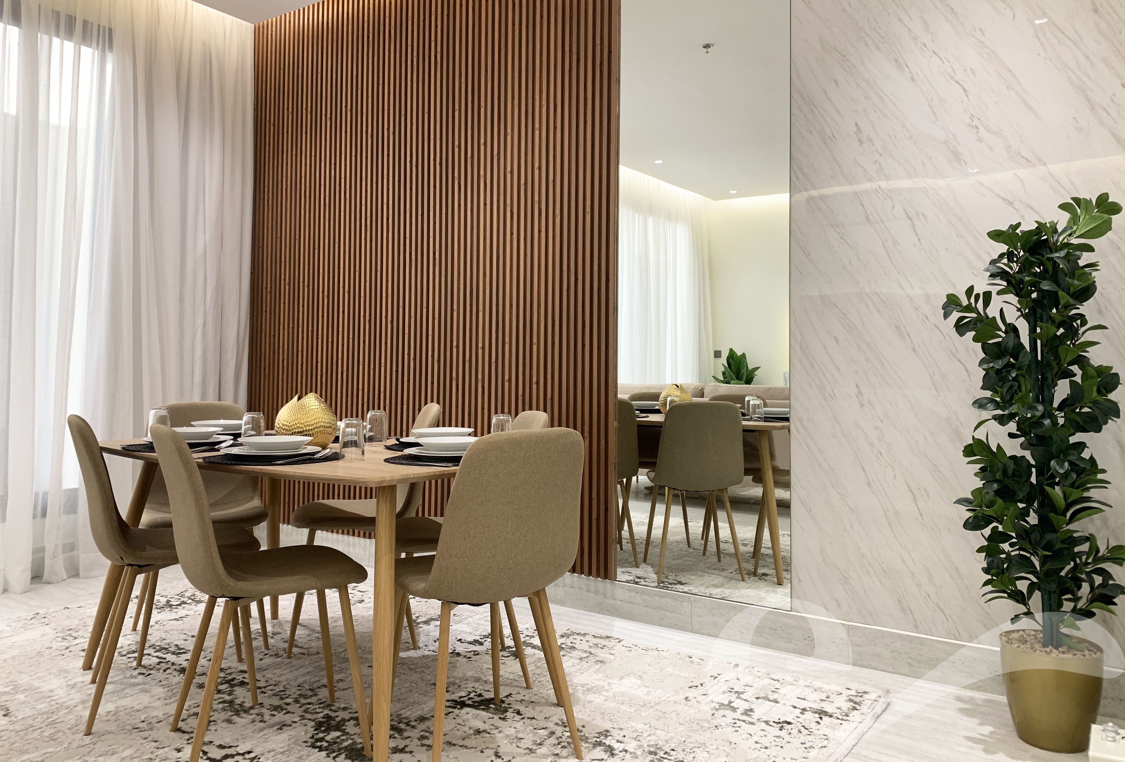 Un comedor moderno con separador de madera, pared de mármol y una planta en maceta.