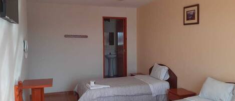 A hotel room with two beds, a small table, a sink, and a framed picture on the wall.