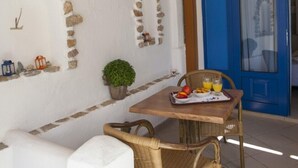 A small outdoor seating area with a table set for breakfast, a blue door, and stone wall decorations. - Dafnis Koufonisia (Naxos)