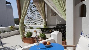 A blue table with a bowl of fruit and a vase, surrounded by white chairs and a white wall. - Dafnis Koufonisia (Naxos)