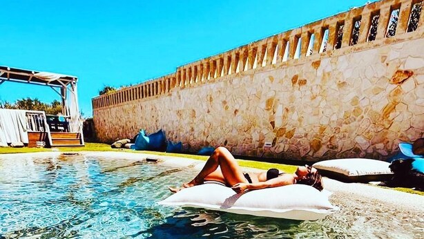 A person lying on a white inflatable float in a clear pool with a stone wall in the background. - DON LEONARDO PRIVATE POOL VILLAS (Polignano a Mare)