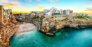Rannikkokaupunki, jossa on historiallisia rakennuksia, kivinen rantaviiva ja kirkas turkoosinsininen vesi.