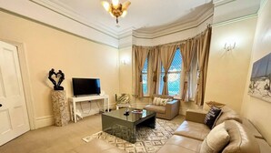 A living room with a sofa, a coffee table, a TV on a stand, and a window with curtains. - Subiaco Heritage House "Gem"! (Shenton Park)