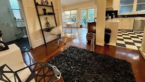 A spacious living area with a large black rug, a dining table with chairs, and a kitchen with checkered flooring. - Subiaco Heritage House "Gem"! (Shenton Park)