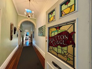 A hallway with a chandelier, a stained glass sign reading "Sutton Lodge," and a wooden headboard.
