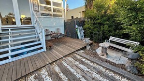 A wooden deck with outdoor furniture, a stone bench, and a fenced garden area. - Subiaco Heritage House "Gem"! (Shenton Park)