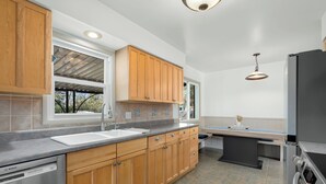 Eine moderne Küche mit Holzausstattung, einem Geschirrspüler von Bosch, einem schwarzen Kühlschrank und einem Fenster mit Blick auf Bäume.