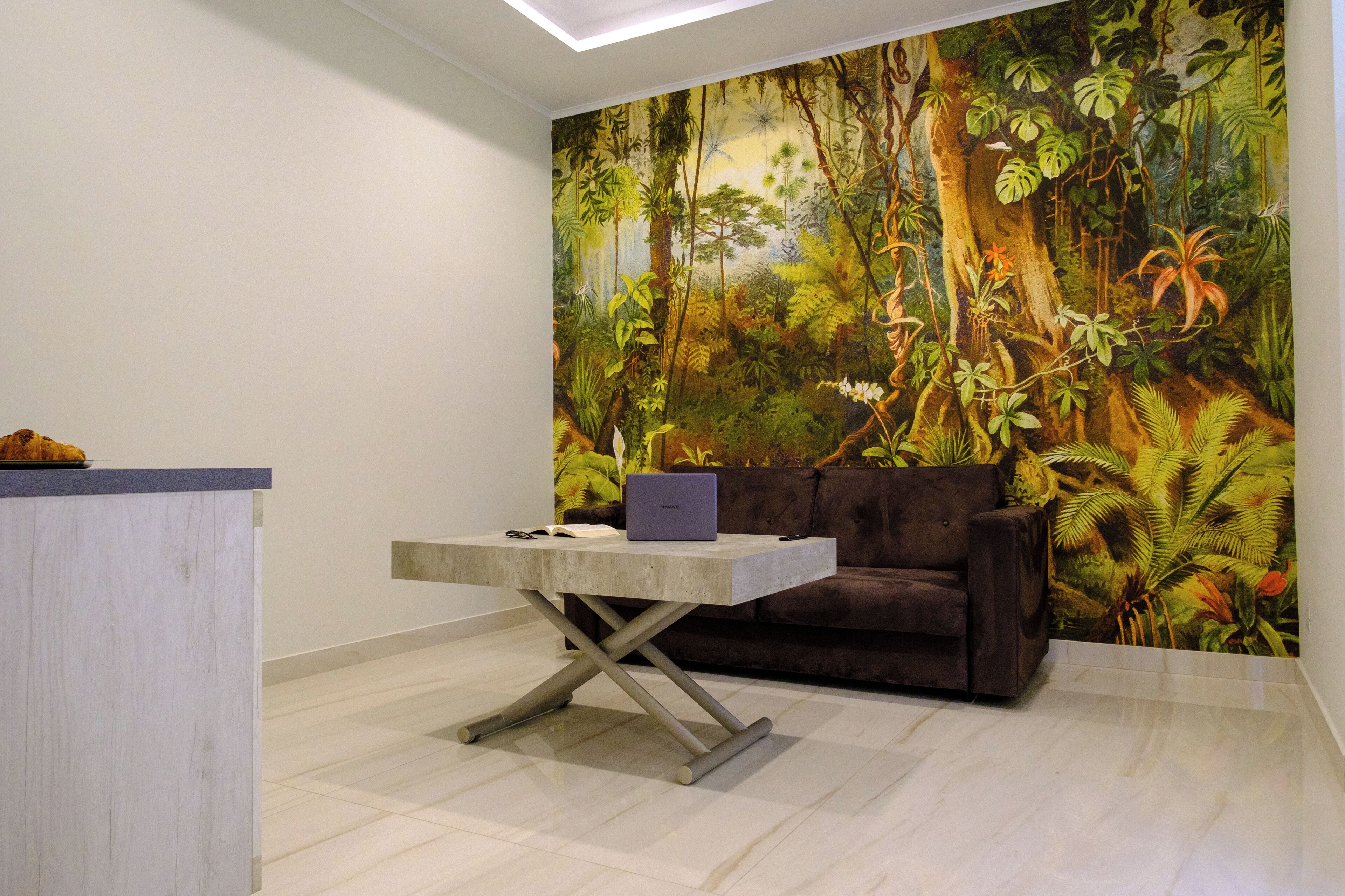 A room with a large mural of a forest, a sofa, a coffee table with a laptop, and a light-colored floor.