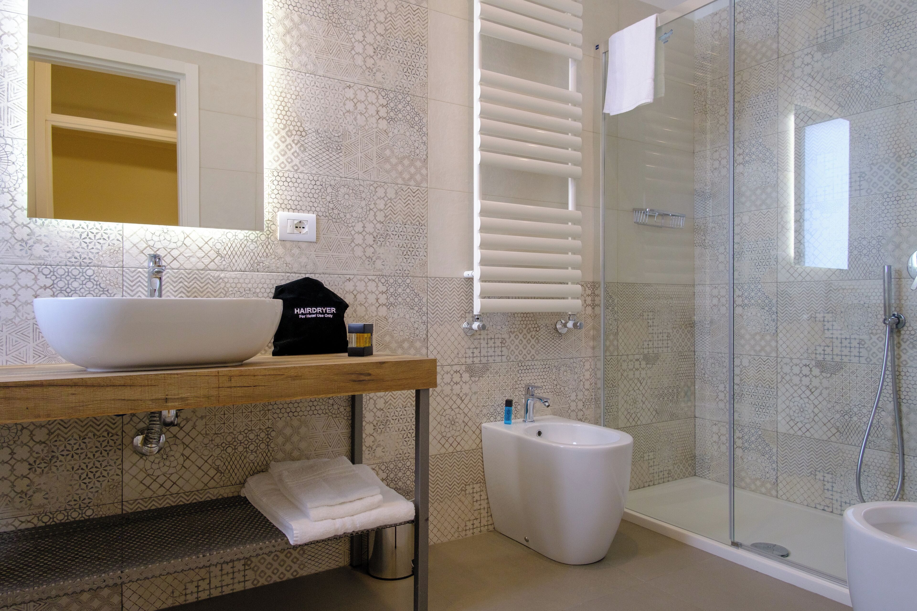 Une salle de bain moderne dotée d’un grand lavabo sur pied, d’un bidet, d’une douche à parois de verre et de carreaux décoratifs.