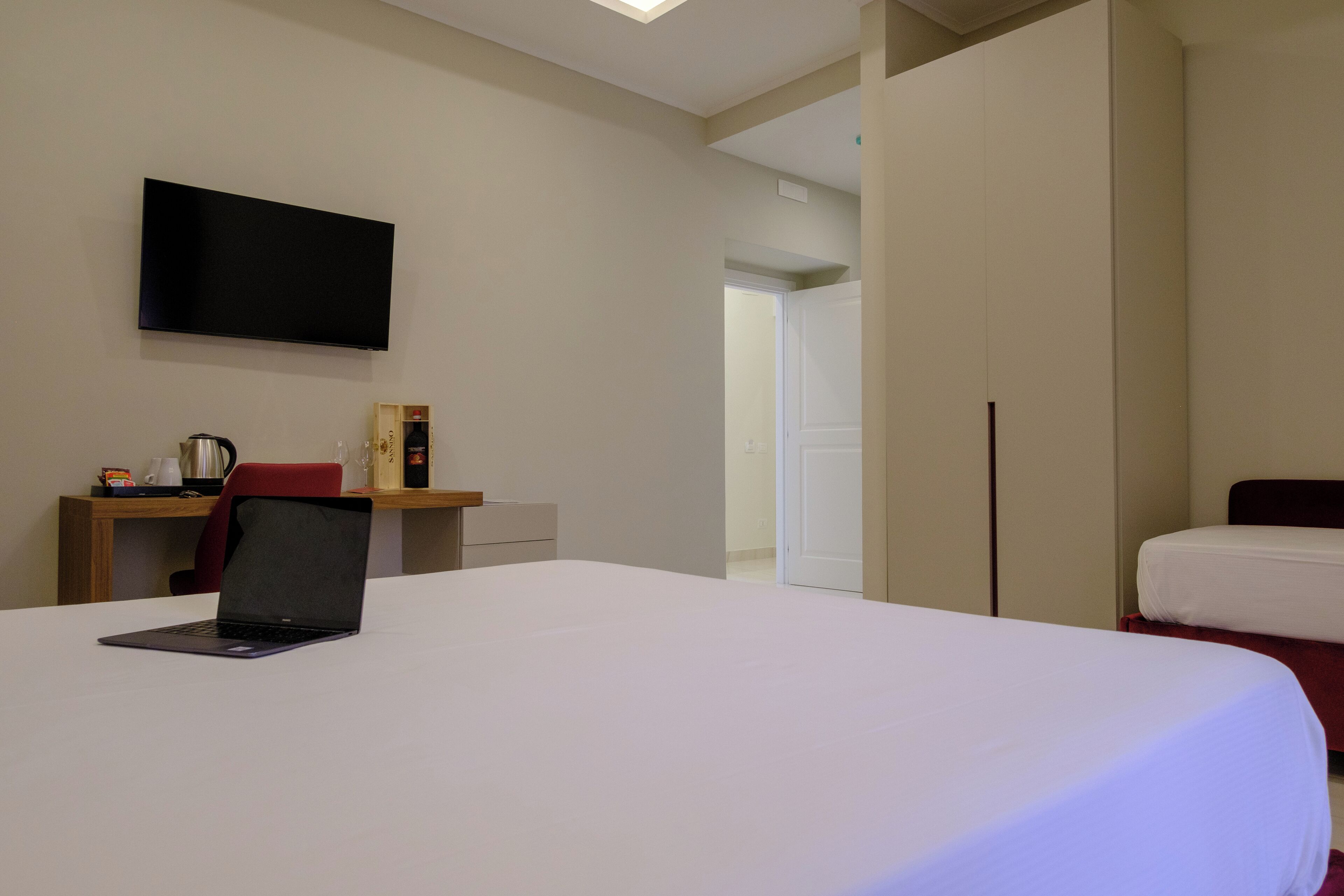 Une chambre d’hôtel comprenant un lit, un bureau avec un ordinateur portable, un téléviseur à écran plat et une porte donnant sur une autre pièce.