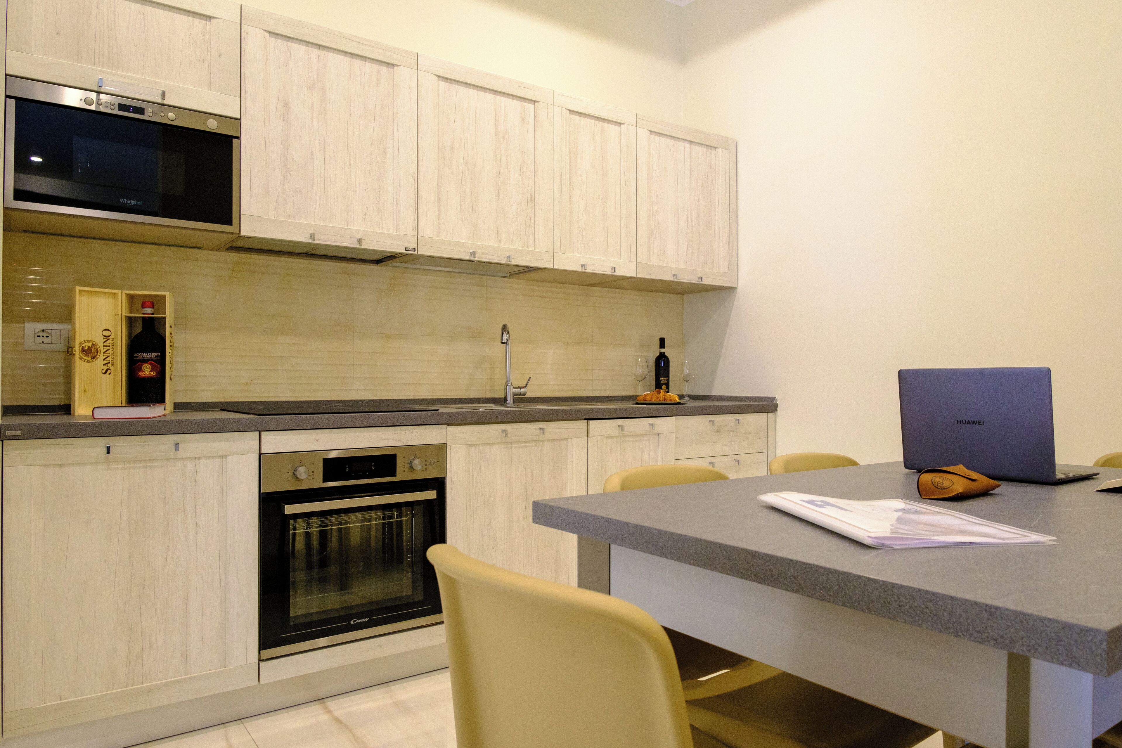 A modern kitchen with wooden cabinets, a built-in oven, a microwave, and a dining area with a table and chairs.