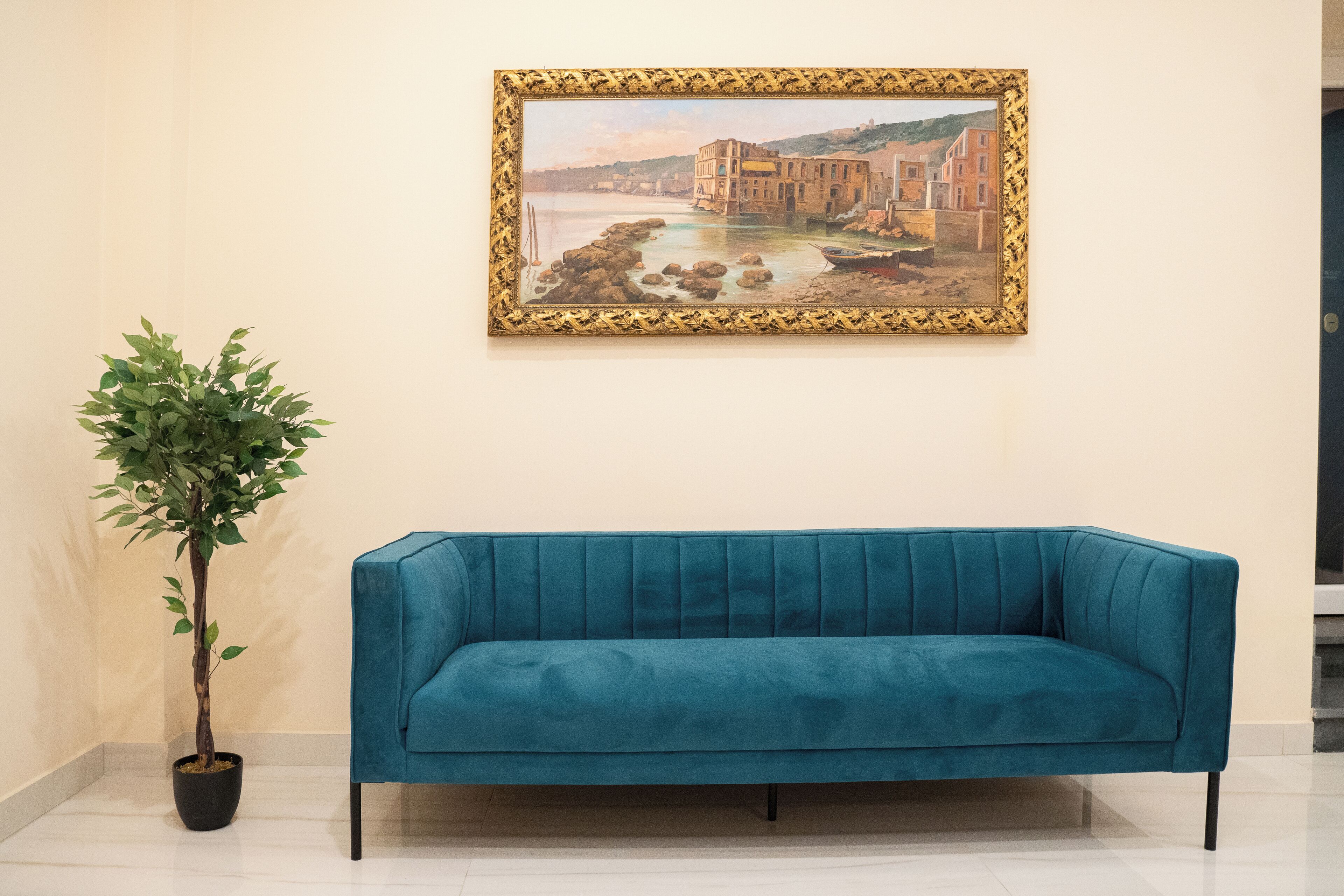 Un canapé de couleur turquoise, une plante en pot et un tableau encadré accroché au mur.