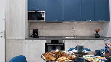 Une cuisine moderne avec des armoires bleues, un four en acier inoxydable et un coin repas avec des chaises bleues et un plateau de pâtisseries.