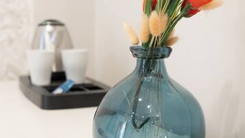 A clear glass vase with orange flowers and pampas grass on a white surface.