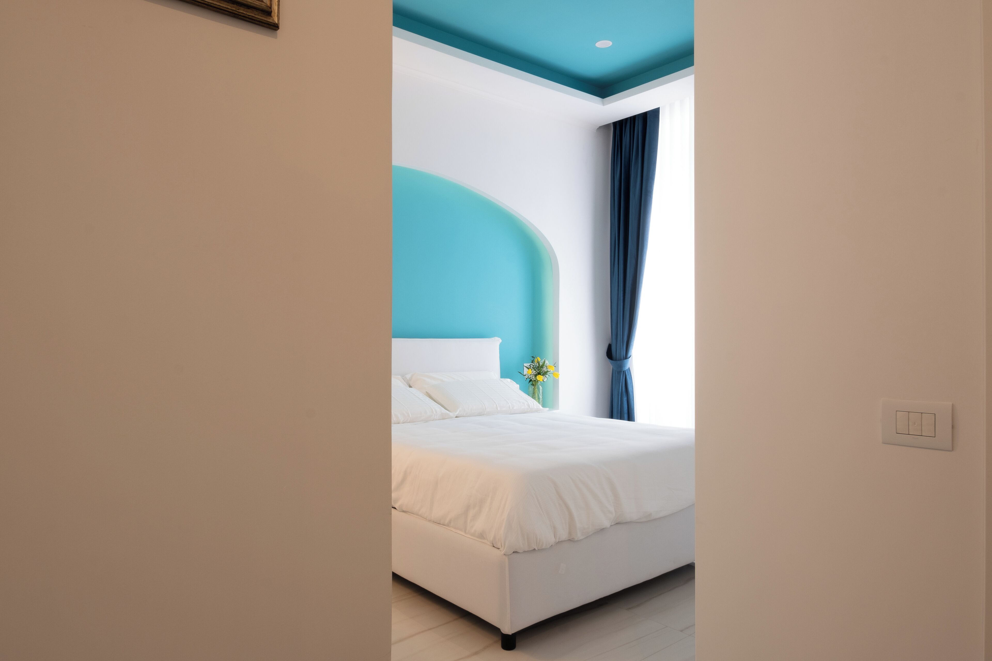 Une chambre moderne avec un lit blanc, un mur d’accent de couleur turquoise et une fenêtre avec des rideaux bleus.