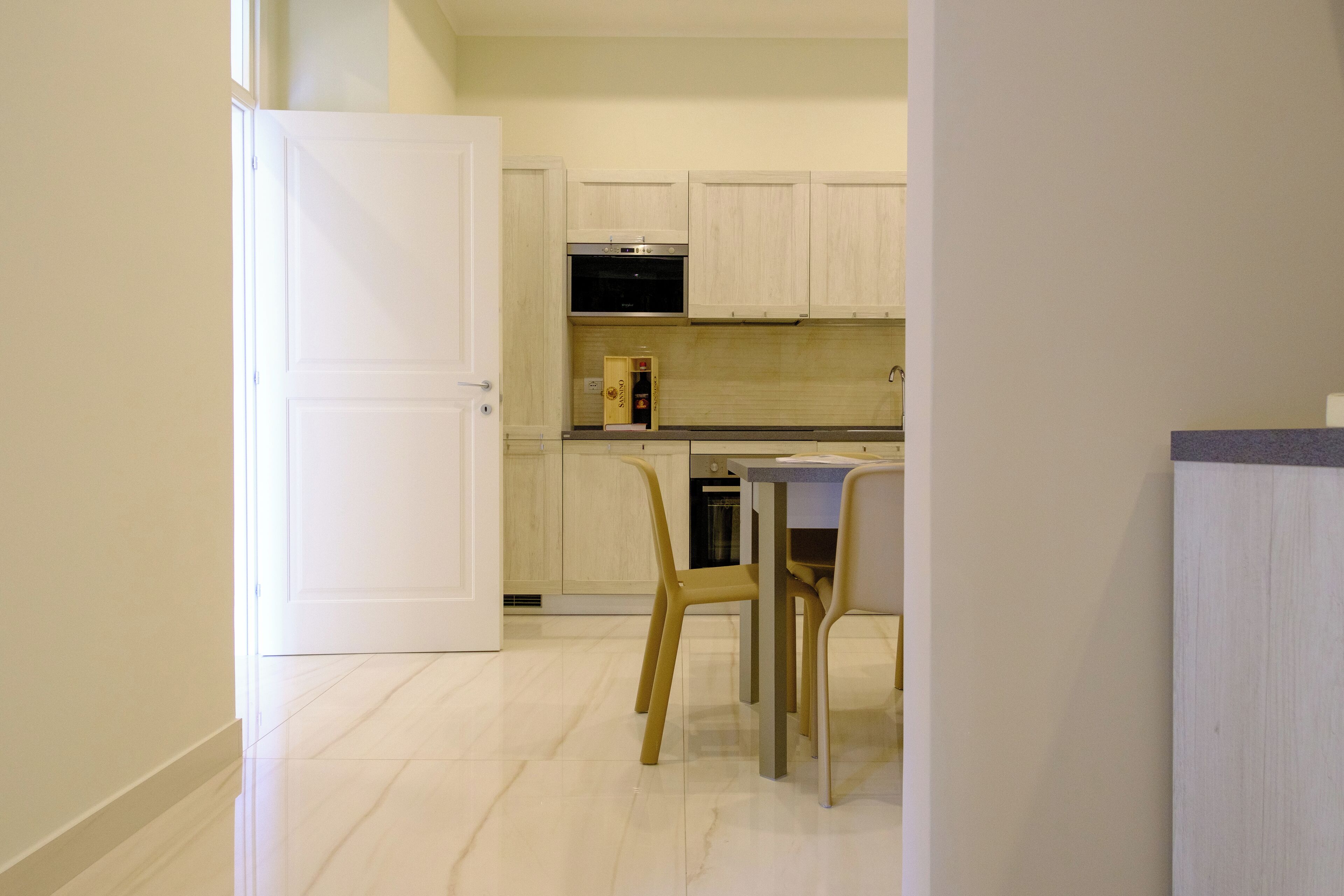 A modern kitchen with light wooden cabinets, a built-in oven, and a dining area with a table and chairs.