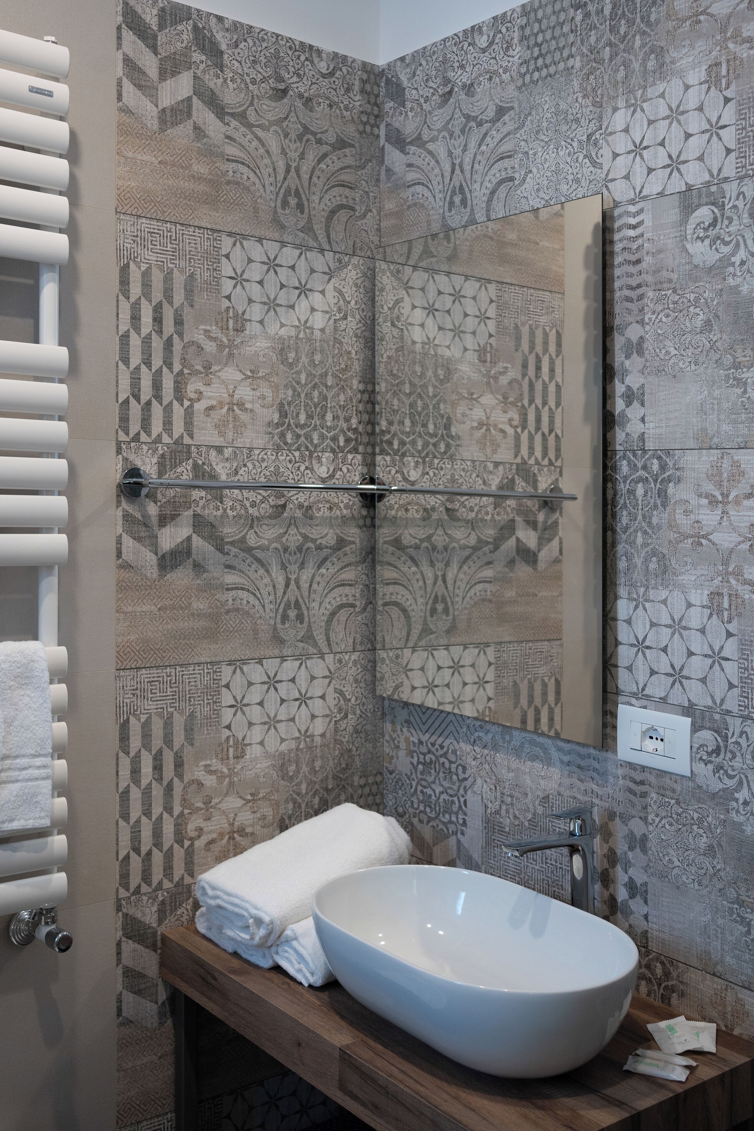 Un bagno con un lavandino ovale grande, un porta asciugamani e piastrelle decorate alle pareti.