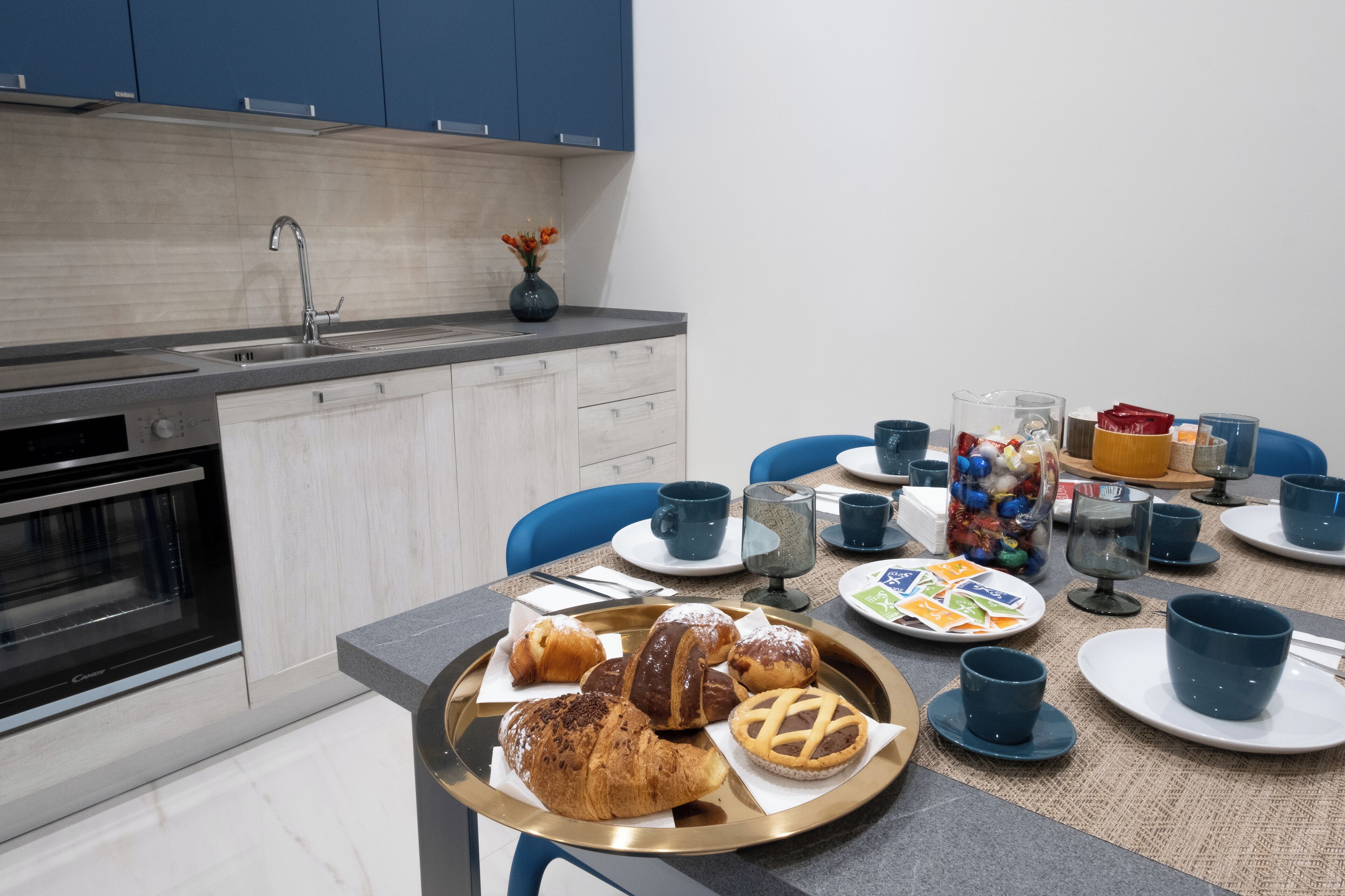 A modern kitchen with a dining table set for breakfast, including pastries and cups.