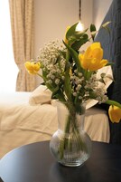 Un jarrón de vidrio transparente con flores amarillas y flores blancas de relleno sobre una mesa redonda.
