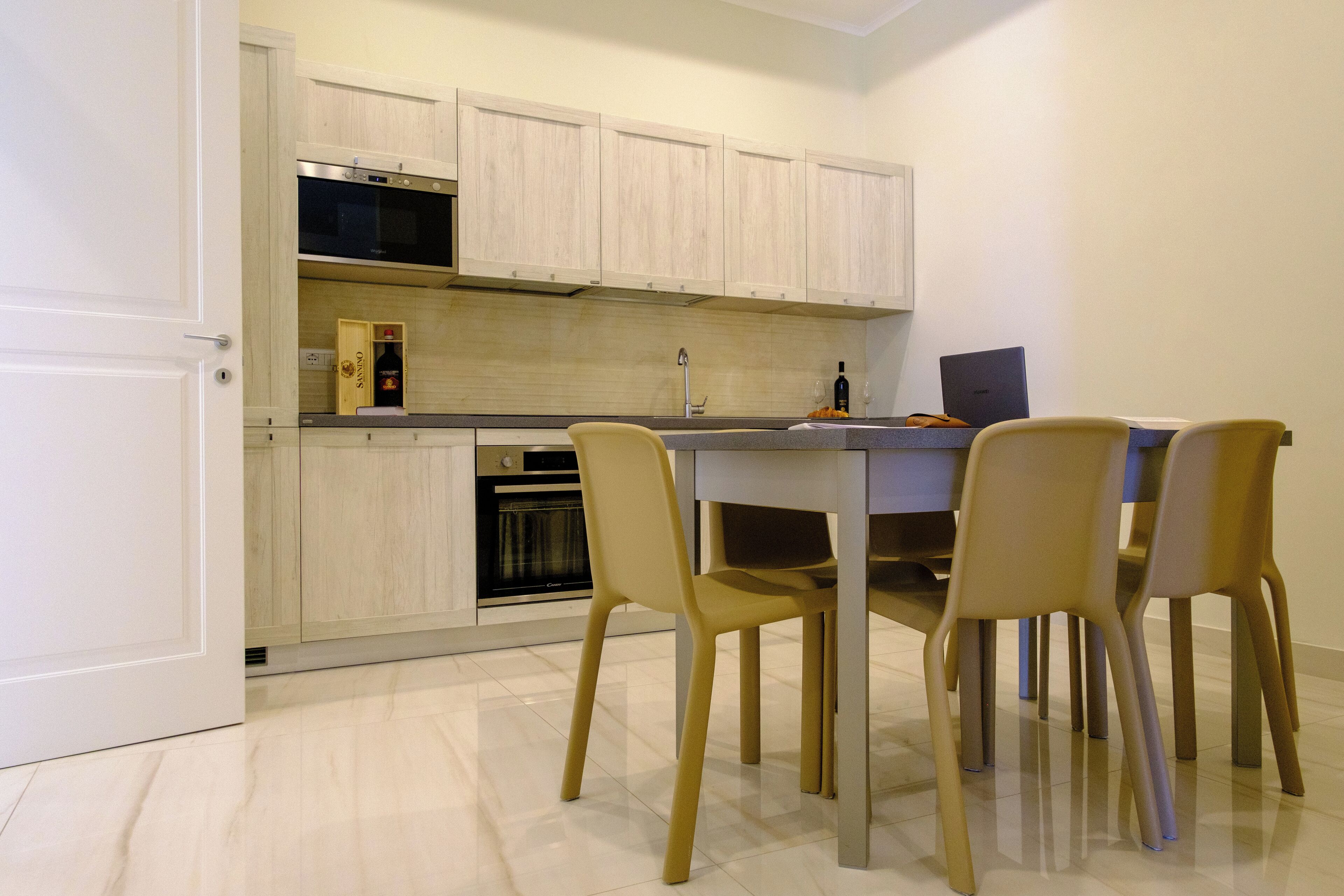 A modern kitchen with light wood cabinets, a built-in oven, and a dining area with four chairs and a table.