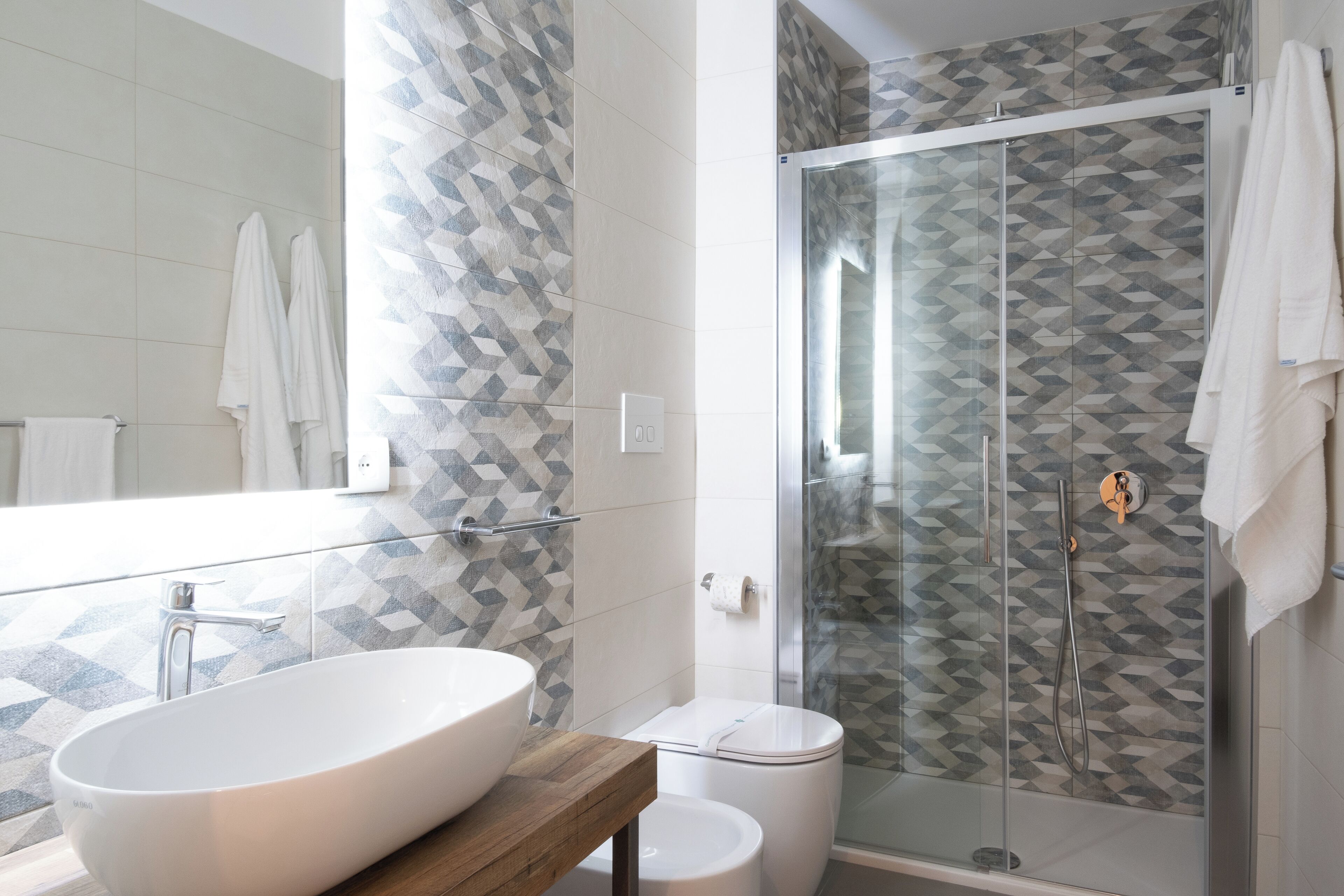 Un baño moderno con un lavabo grande de color blanco, una cabina de ducha de vidrio y baldosas estampadas.