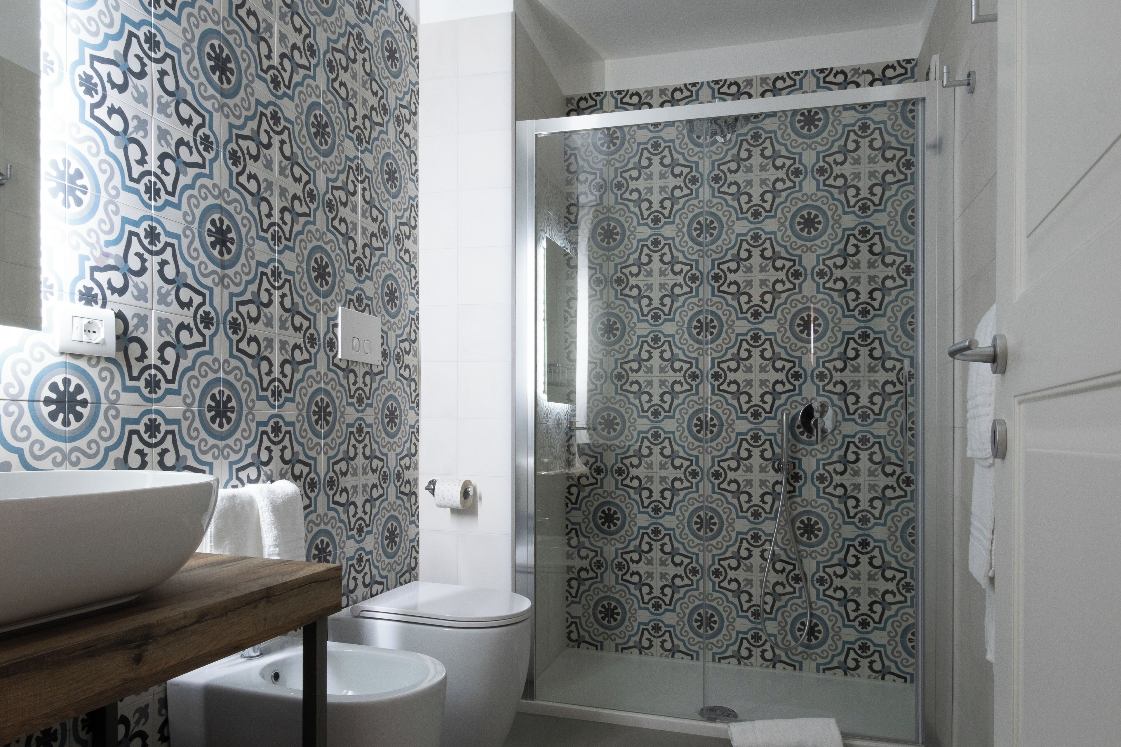A bathroom with patterned tiles, a white sink, and a glass-enclosed shower.