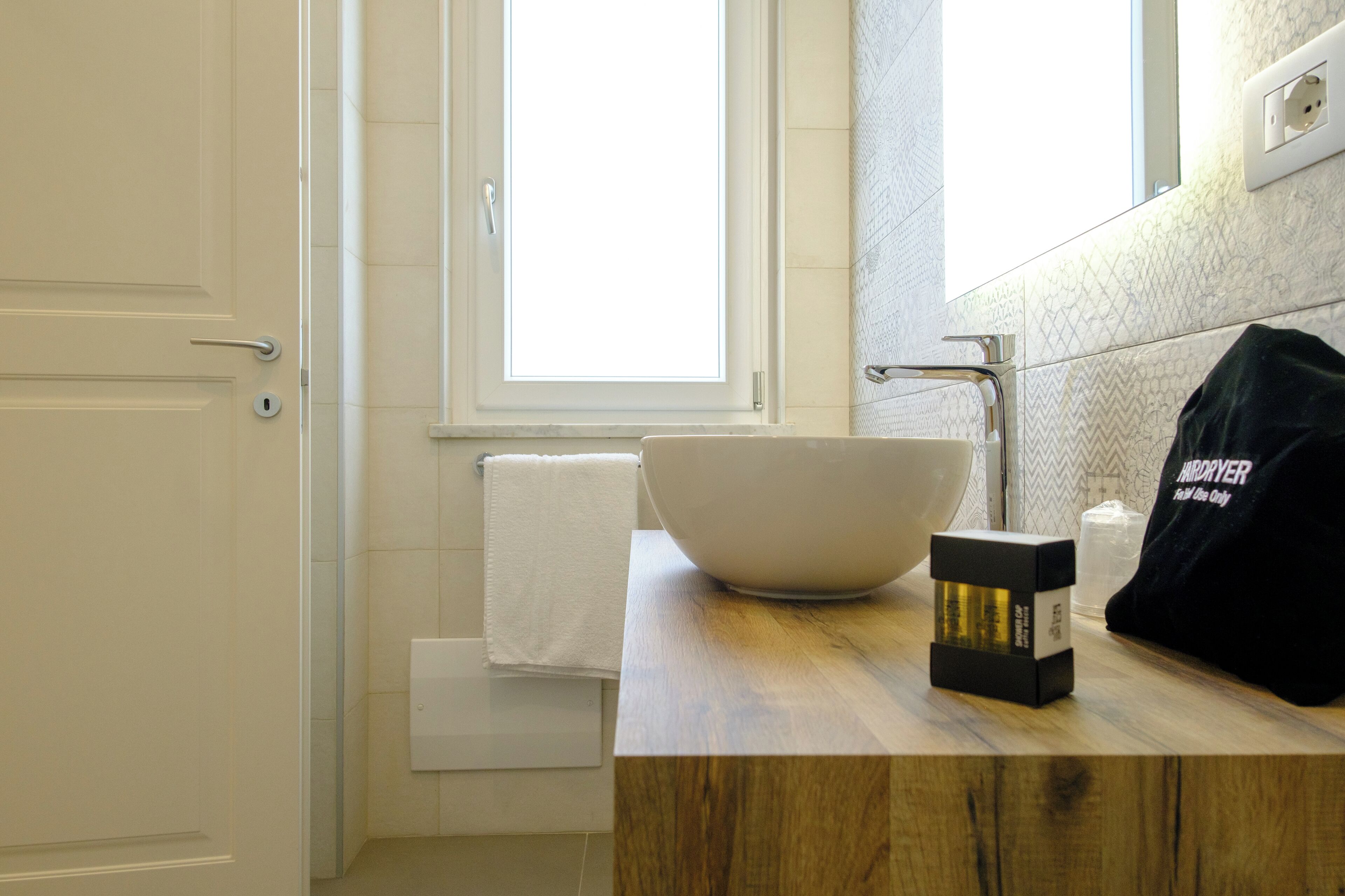 A bathroom with a large white sink, a wooden countertop, a towel, and a black bag with text.