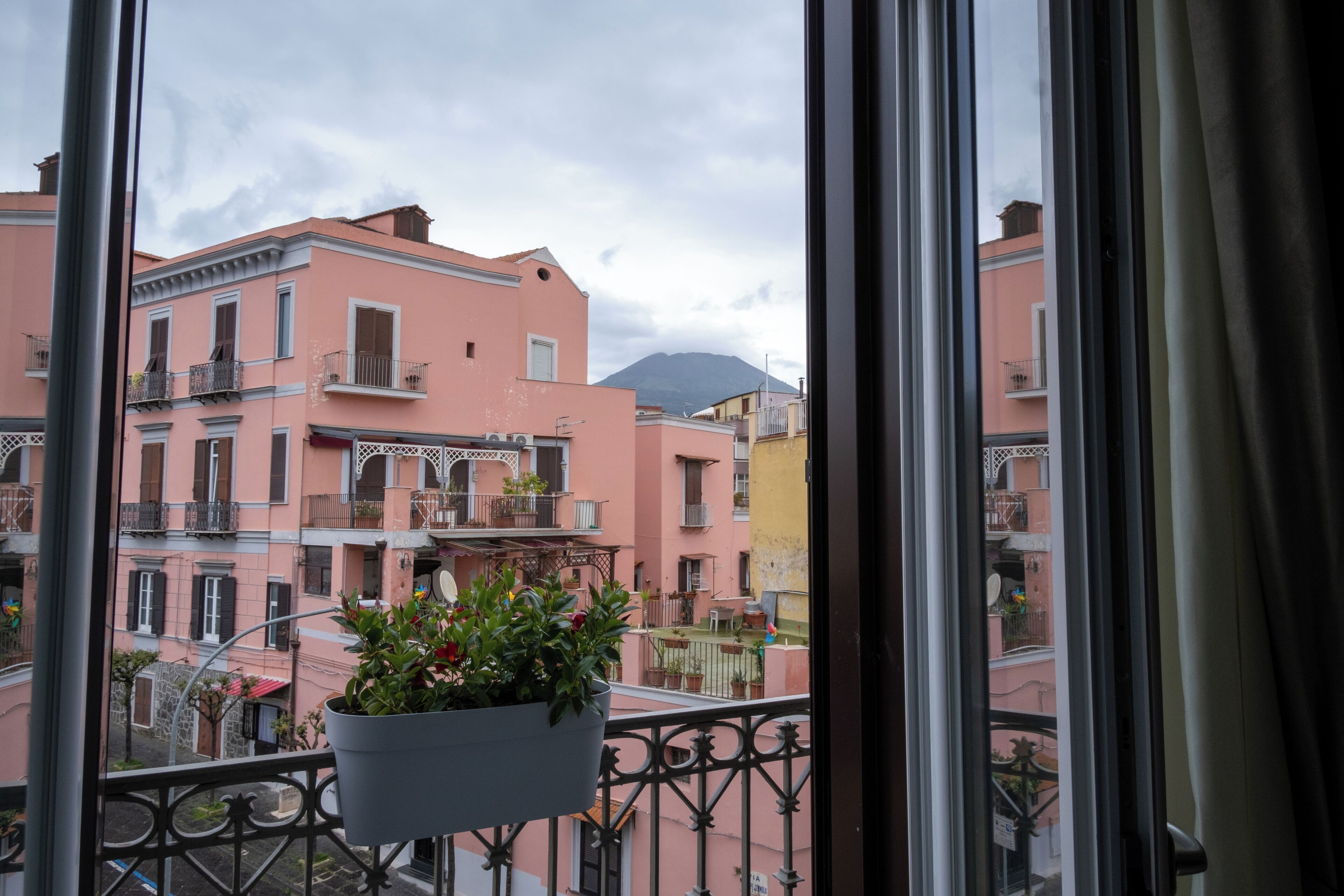 Ein Balkon mit hängenden Pflanzen, rosa Häuser und ein Berg im Hintergrund.