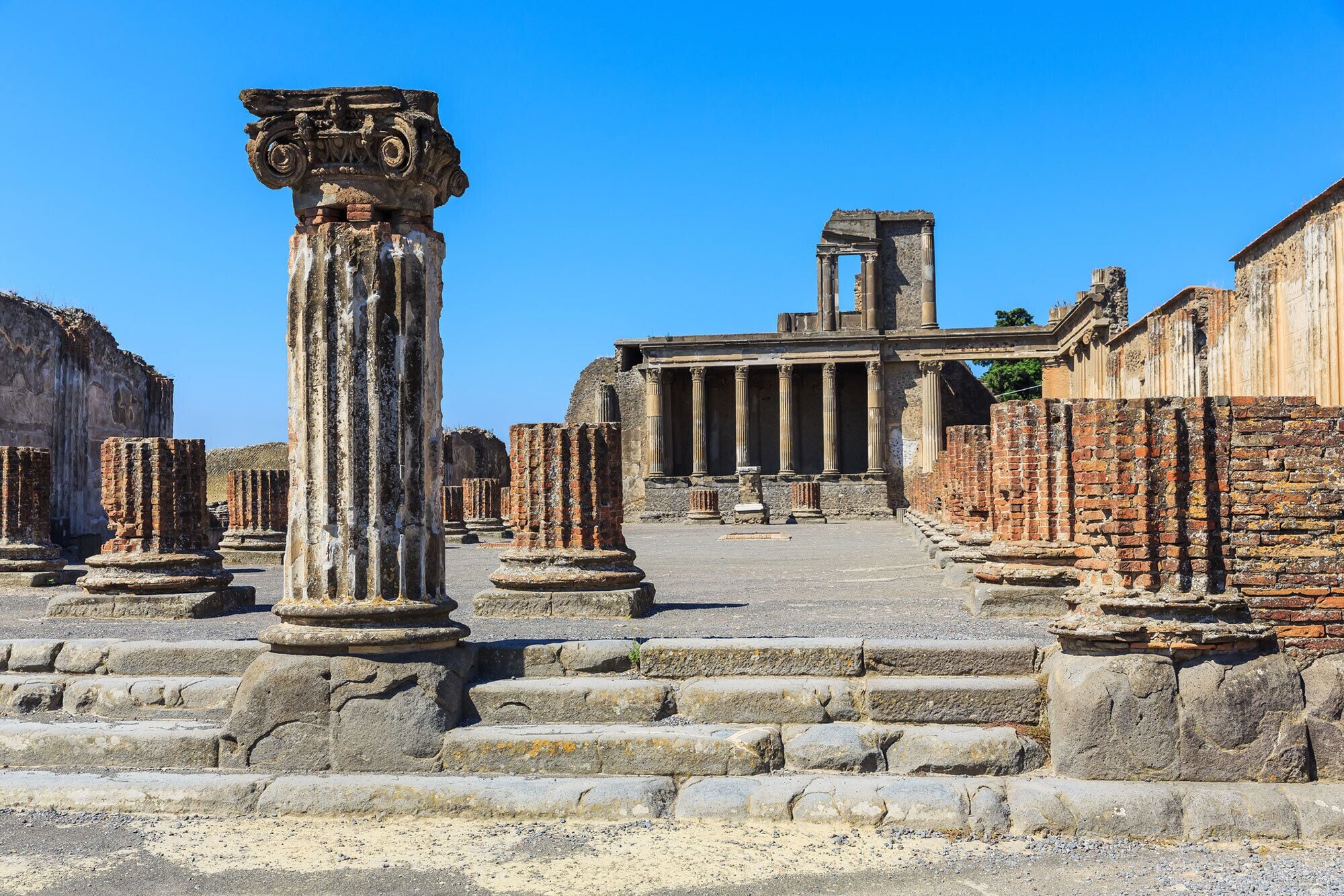 Ancient ruins with columns and steps leading to a temple-like structure.