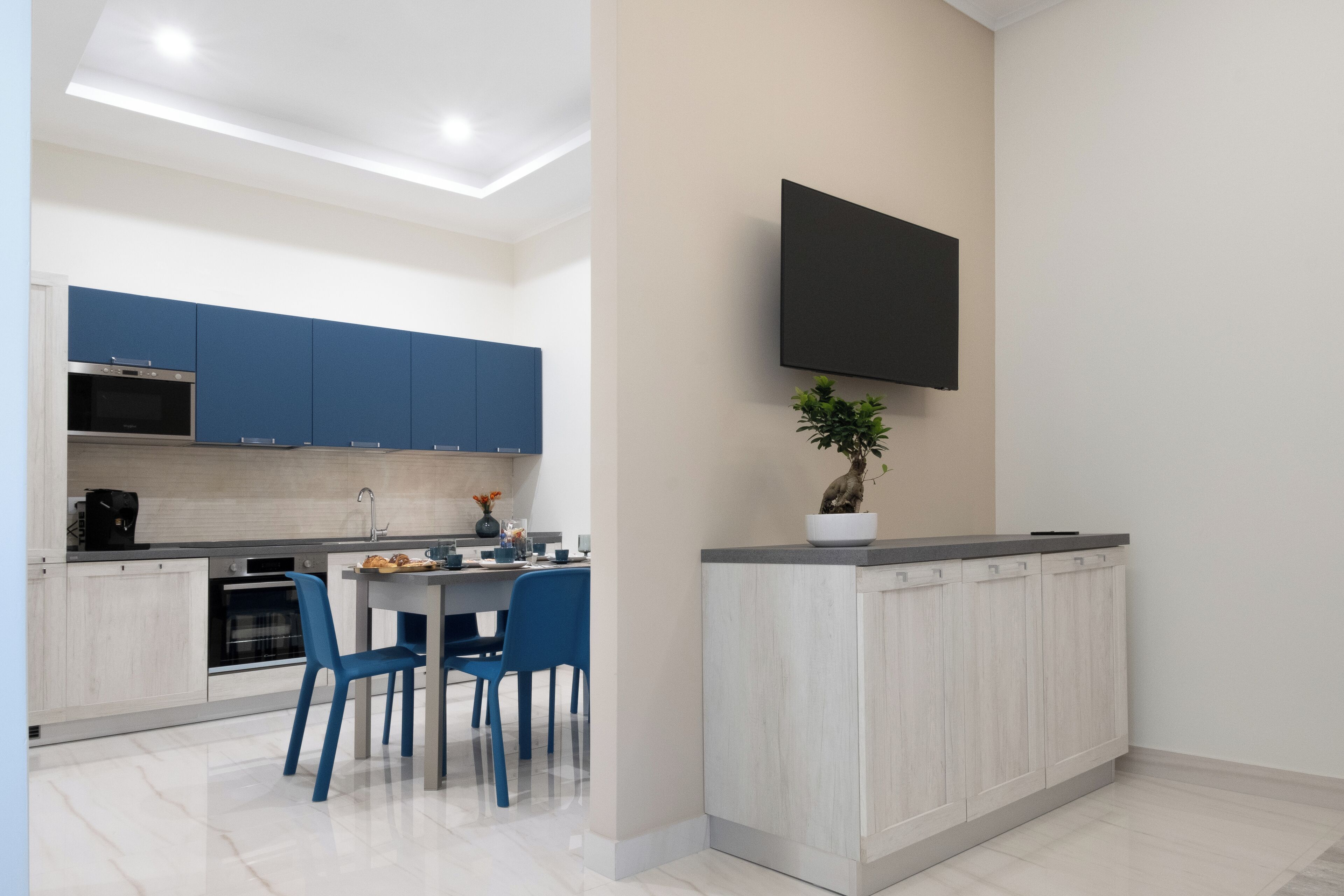 Une cuisine moderne avec des meubles bleus, un coin repas avec des chaises bleues et un téléviseur à écran plat fixé au mur.