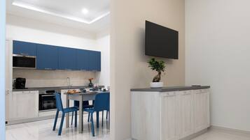 A modern kitchen with blue cabinets, a dining area with blue chairs, and a flat-screen TV mounted on the wall.