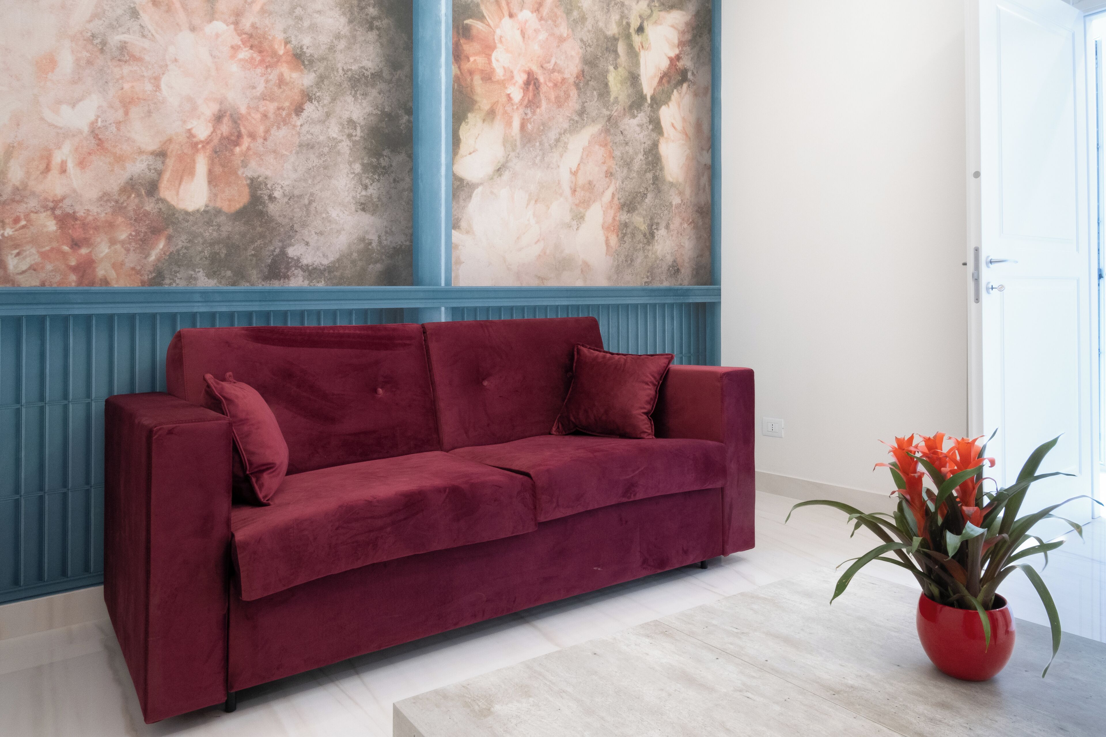 Un sofá rojo en una habitación con paneles inferiores azules y un cuadro grande con motivos florales en la pared.