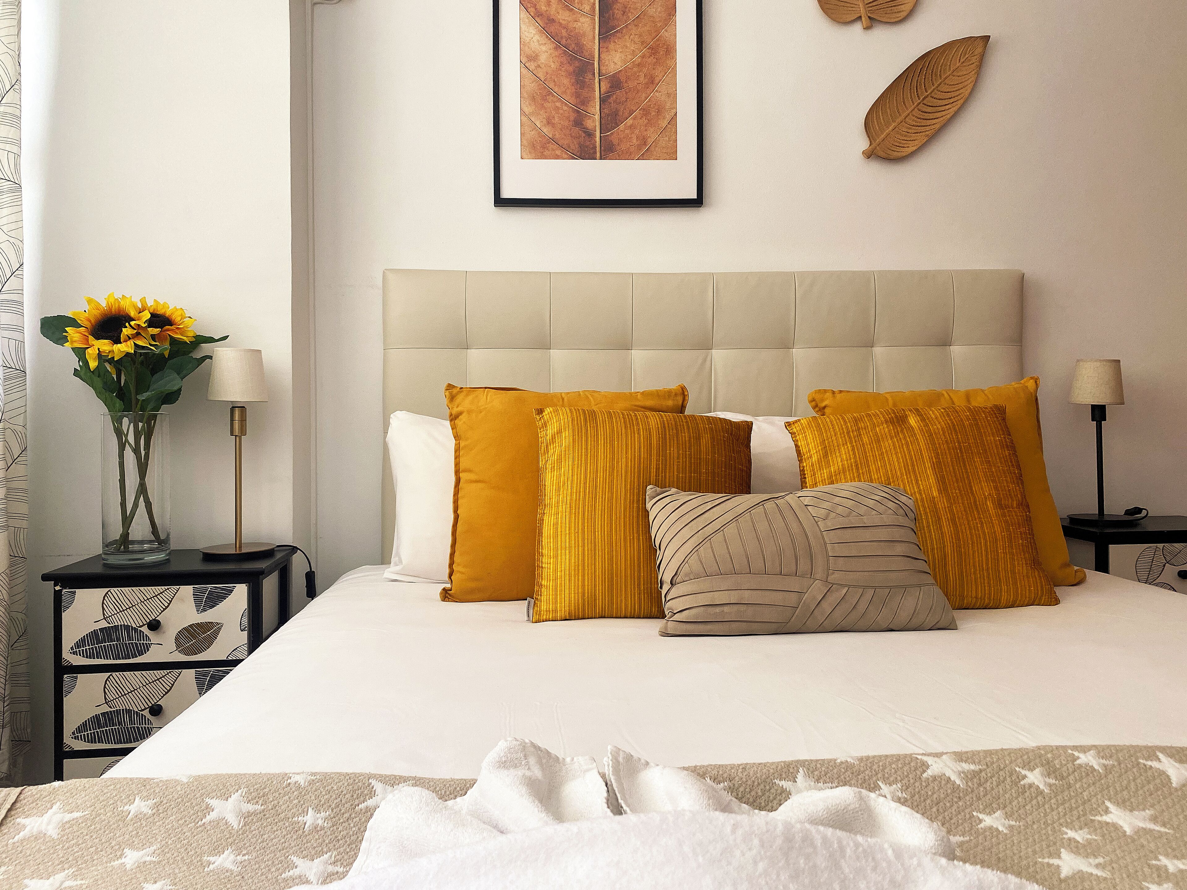 A neatly made bed with a tufted headboard, a vase with sunflowers, and a framed artwork on the wall.