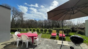 An outdoor patio with a table set for two, a barbecue grill, and a large umbrella providing shade. - Maison Récente Avec Tous les Équipements Traditionnels Très Bien Situé (Plouër-sur-Rance)