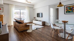 A modern living room with a brown sofa, a glass dining table with white chairs, a TV on the wall, and a ceiling fan. - Apt. dos Correios, a short walk to the town center (Lagos)