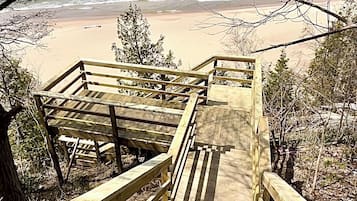 Un escalier en bois mène à une plage où l’eau est d’un bleu cristallin et le rivage est sablonneux.