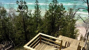Une terrasse en bois qui mène à une plage bordée d’une eau turquoise et sous un ciel dégagé.