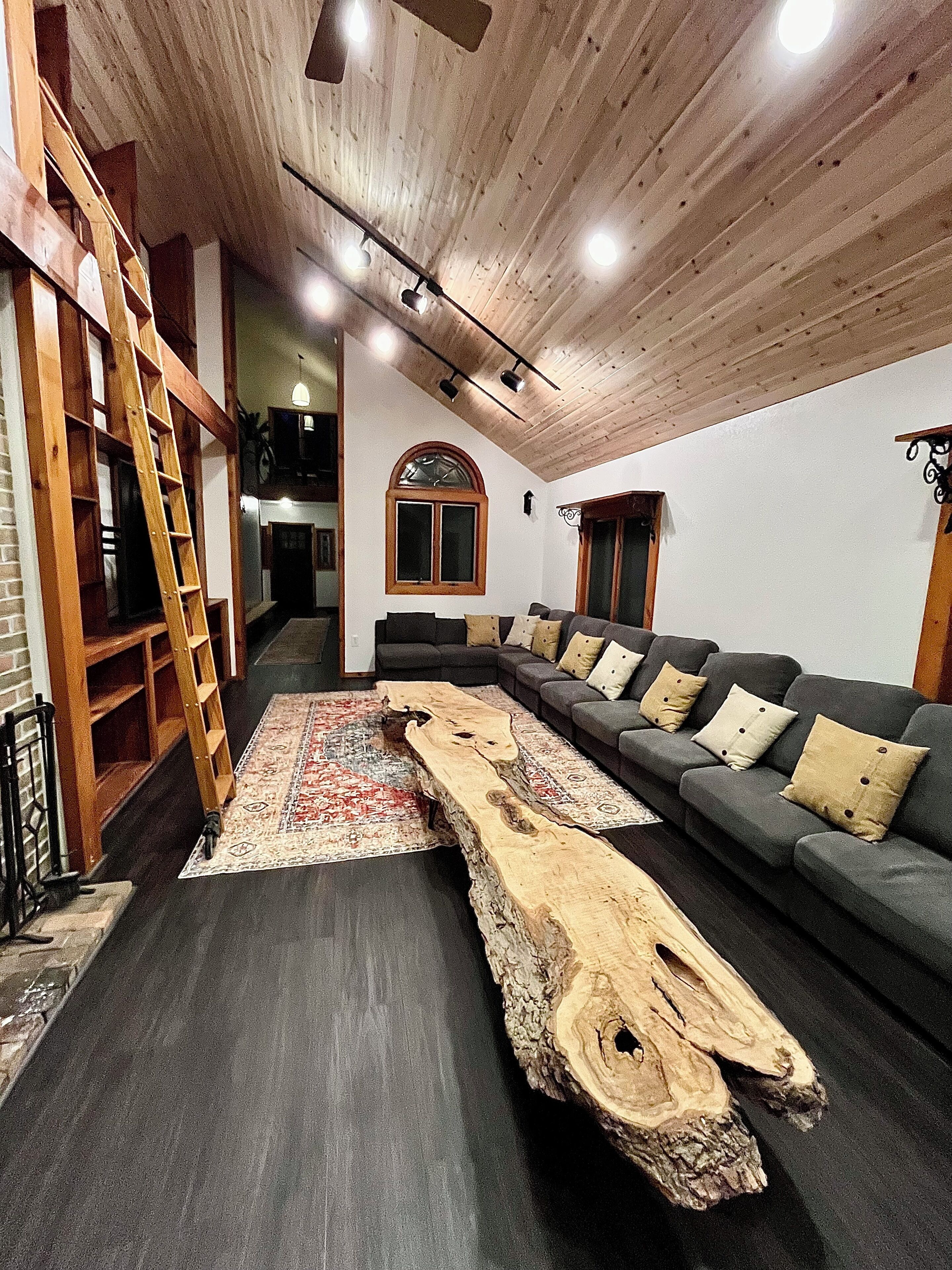 A modern living room with a wooden ceiling, a large sectional sofa, and a unique wooden coffee table.