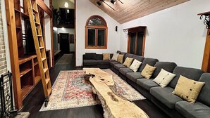 Un salon moderne avec un plafond en bois, un grand canapé d’angle et une table basse en bois au design original.