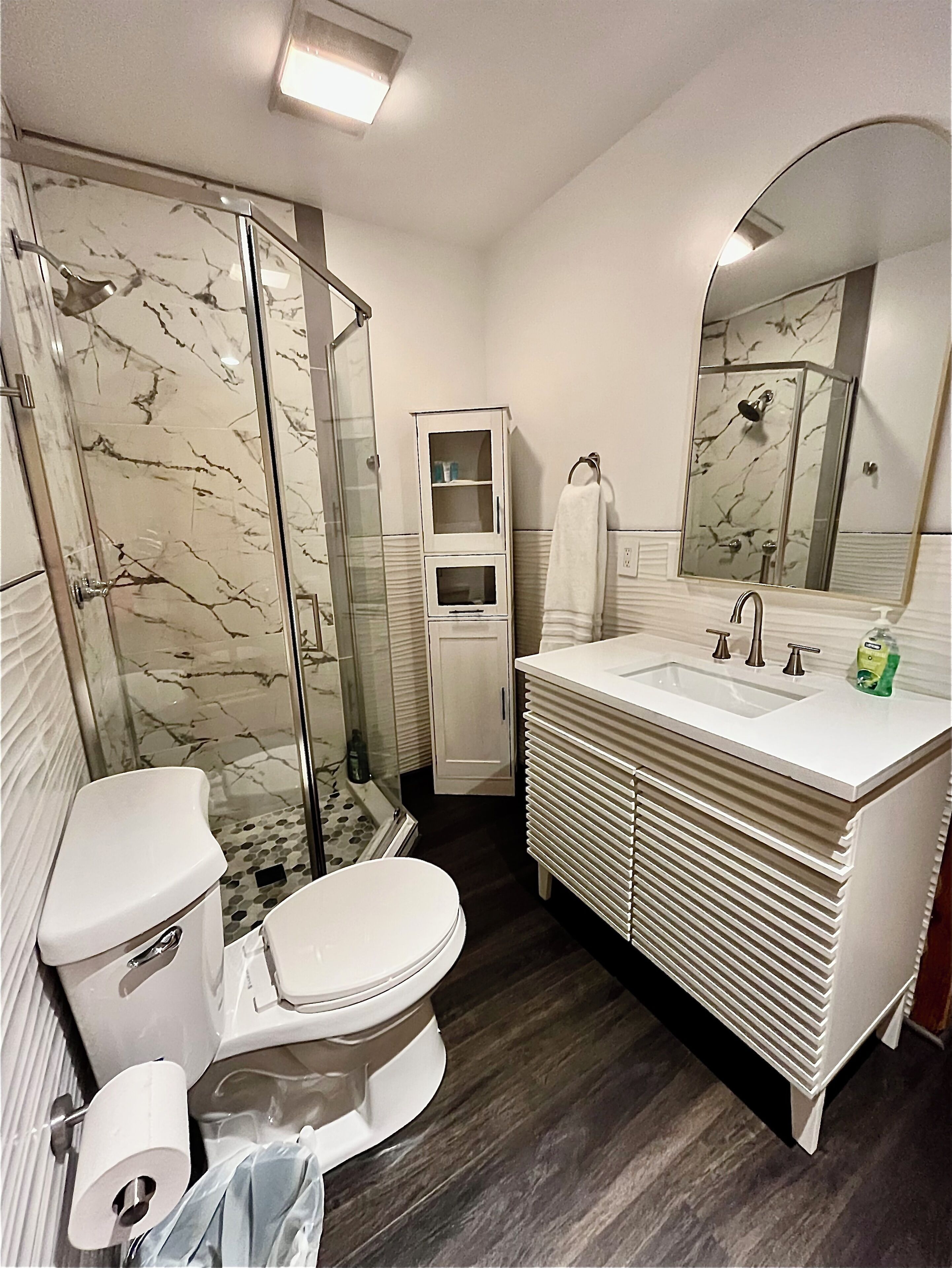 A bathroom with a glass-enclosed shower, a toilet, a sink with a mirror, and a cabinet.