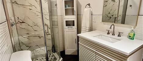 A bathroom with a glass-enclosed shower, a toilet, a sink with a mirror, and a cabinet.