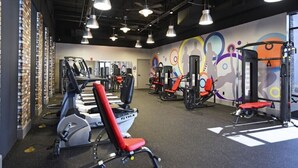 A gym with various exercise equipment, including treadmills and weight machines, and a colorful mural on the wall.